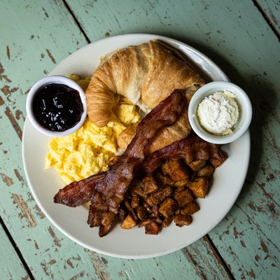 Classic Breakfast Plate with scrambled eggs, bacon, potatoes and a croissant.