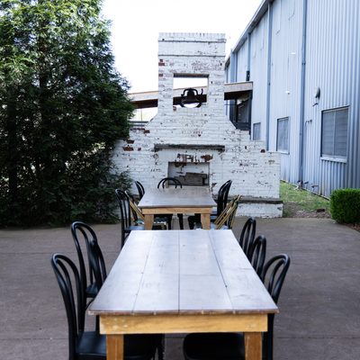 Outdoor patio with long wooden tables and a white brick fireplace.
